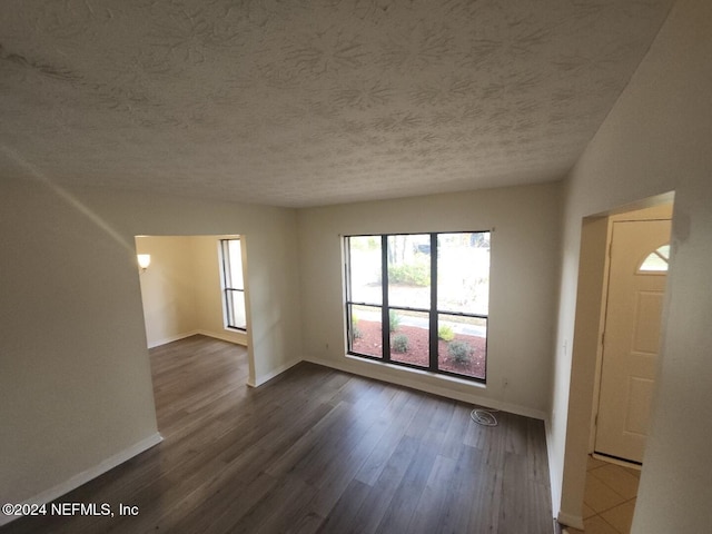 spare room with dark wood-style flooring, a textured ceiling, and baseboards