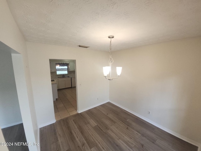 unfurnished dining area featuring a textured ceiling, a notable chandelier, wood finished floors, visible vents, and baseboards