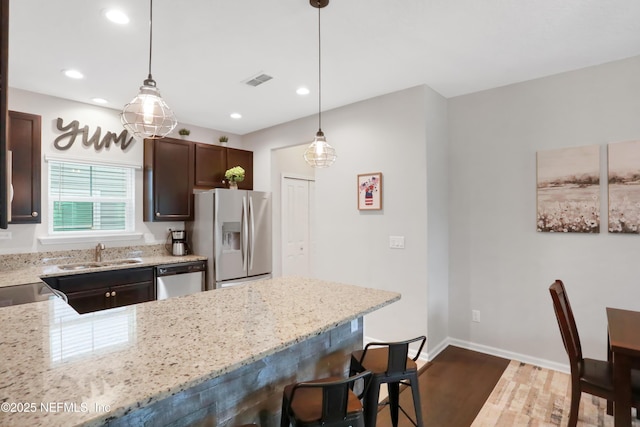 kitchen with appliances with stainless steel finishes, hanging light fixtures, a kitchen bar, light stone counters, and sink