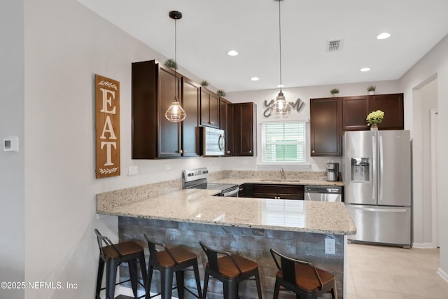 kitchen featuring decorative light fixtures, light stone counters, kitchen peninsula, and appliances with stainless steel finishes