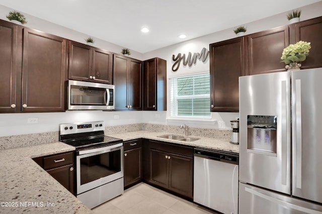 kitchen with light stone countertops, appliances with stainless steel finishes, dark brown cabinetry, and sink