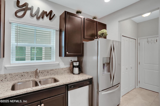 kitchen with stainless steel appliances, dark brown cabinetry, sink, and light stone countertops