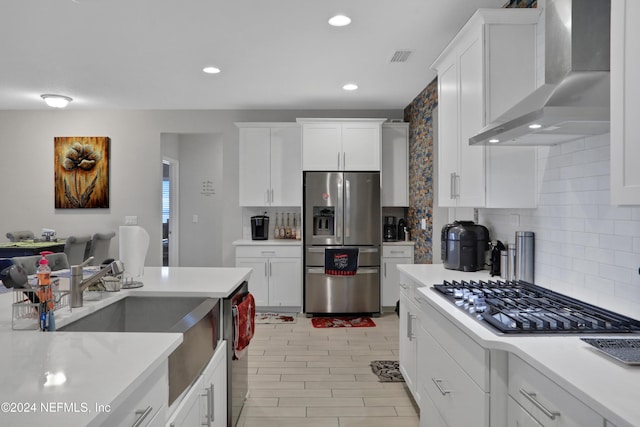 kitchen with decorative backsplash, stainless steel appliances, wall chimney range hood, light hardwood / wood-style flooring, and white cabinets