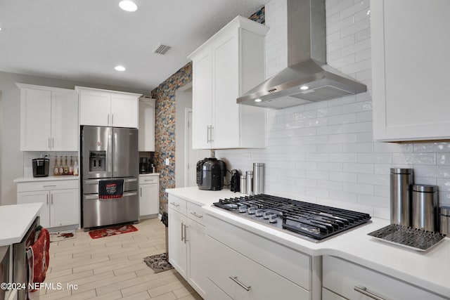 kitchen featuring white cabinets, decorative backsplash, wall chimney exhaust hood, and appliances with stainless steel finishes