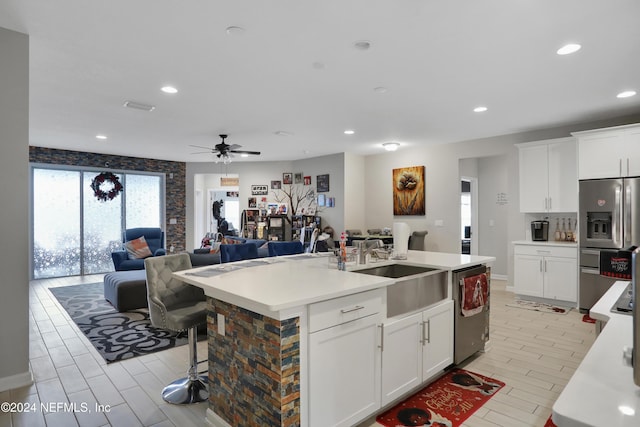 kitchen with ceiling fan, a center island with sink, white cabinets, and appliances with stainless steel finishes