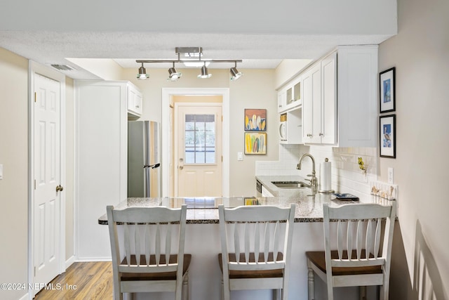 kitchen with stainless steel fridge, light stone counters, white cabinetry, and sink