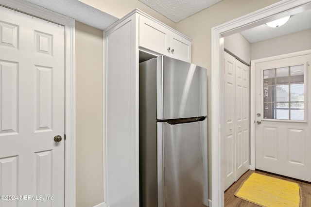 kitchen with white cabinets, stainless steel fridge, a textured ceiling, and wood-type flooring