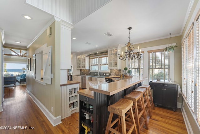 kitchen featuring kitchen peninsula, a kitchen breakfast bar, wooden counters, crown molding, and a notable chandelier