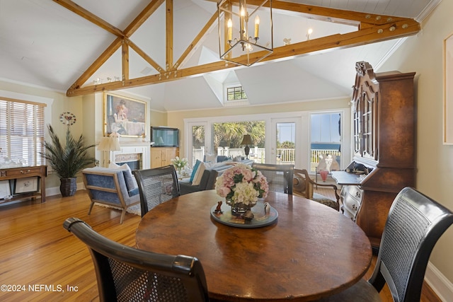 dining area featuring beam ceiling, wood-type flooring, high vaulted ceiling, a fireplace, and a chandelier