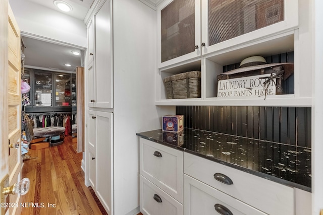 bar with dark stone countertops, white cabinetry, and light hardwood / wood-style floors