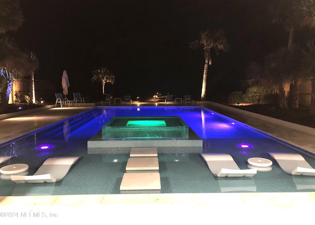 pool at night with an in ground hot tub and a patio