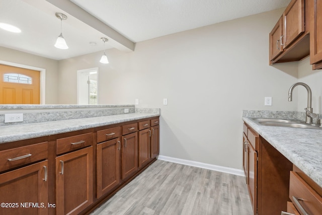 kitchen with light stone countertops, sink, beam ceiling, light hardwood / wood-style floors, and hanging light fixtures