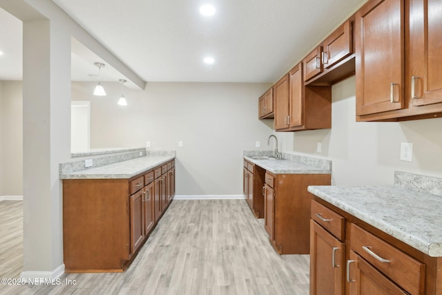 kitchen with light stone counters, sink, hanging light fixtures, and light hardwood / wood-style flooring