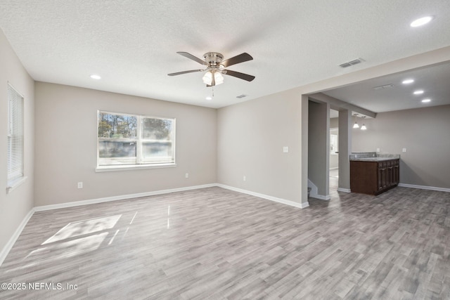 unfurnished living room with ceiling fan, a textured ceiling, and light wood-type flooring