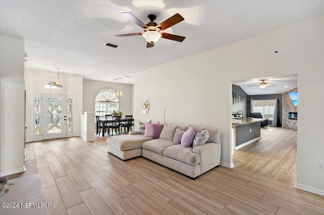 living room with a stone fireplace, ceiling fan, sink, and a textured ceiling