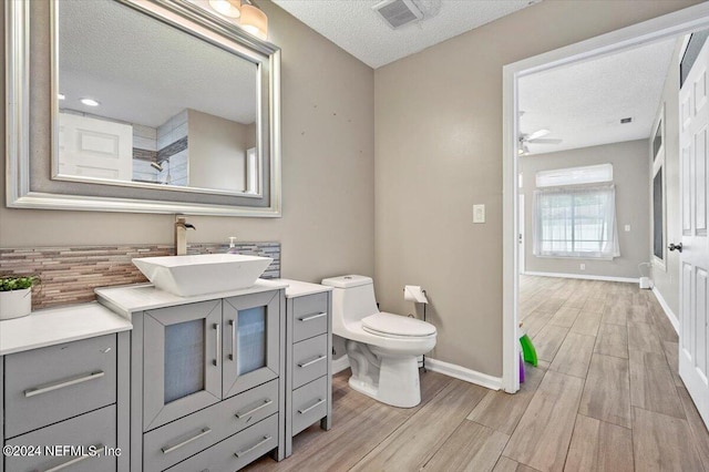 bathroom featuring ceiling fan, wood-type flooring, a textured ceiling, toilet, and vanity