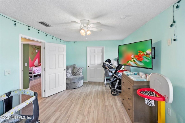 recreation room with ceiling fan, a textured ceiling, and light hardwood / wood-style flooring