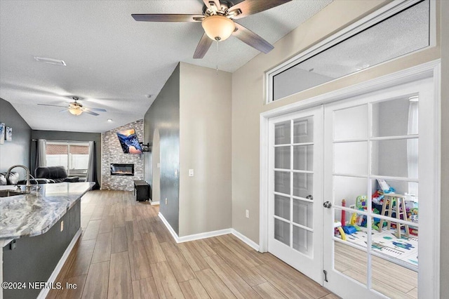 kitchen featuring ceiling fan, french doors, sink, a stone fireplace, and a textured ceiling