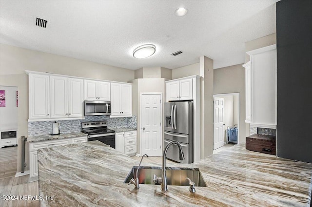 kitchen with white cabinetry, sink, stainless steel appliances, light stone counters, and backsplash