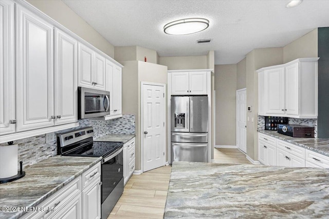 kitchen with white cabinets, a textured ceiling, tasteful backsplash, light stone counters, and stainless steel appliances