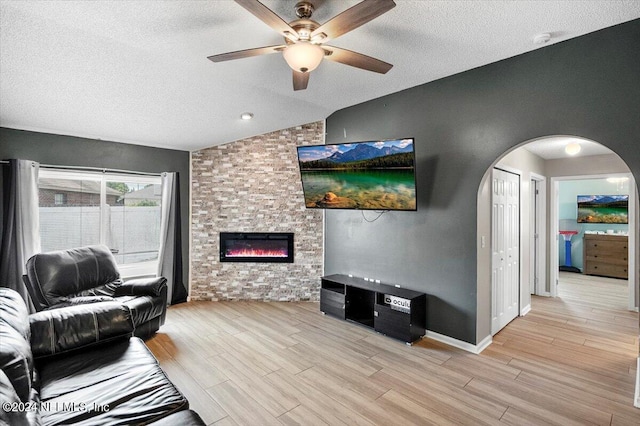 living room with a textured ceiling, vaulted ceiling, ceiling fan, light hardwood / wood-style flooring, and a fireplace