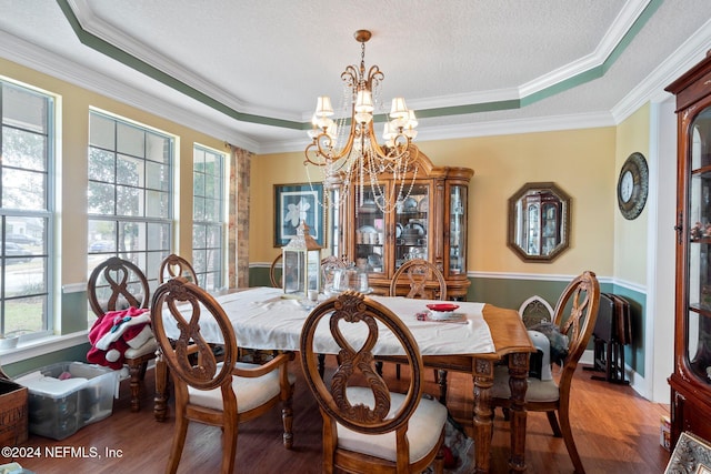 dining room with a chandelier, hardwood / wood-style flooring, a raised ceiling, and ornamental molding