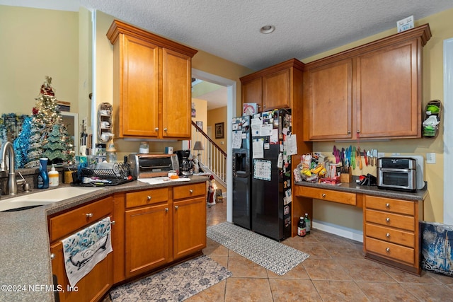 kitchen featuring light tile patterned flooring, a textured ceiling, black refrigerator with ice dispenser, and sink