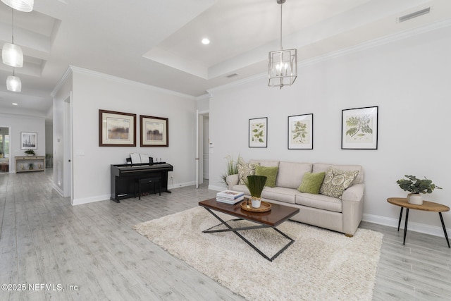 living room featuring a raised ceiling, ornamental molding, a chandelier, and light hardwood / wood-style floors