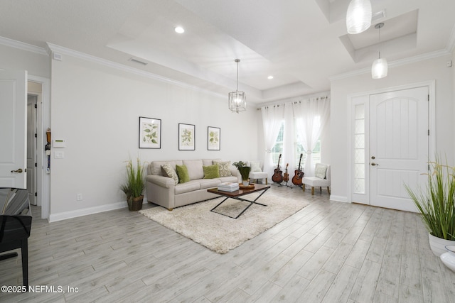 living room with crown molding, a raised ceiling, a chandelier, and light wood-type flooring