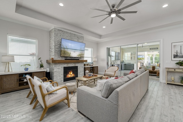 living room featuring a raised ceiling, crown molding, a fireplace, and light hardwood / wood-style floors