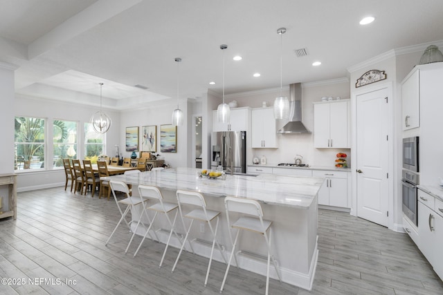 kitchen featuring a breakfast bar, white cabinetry, a large island with sink, stainless steel appliances, and wall chimney range hood