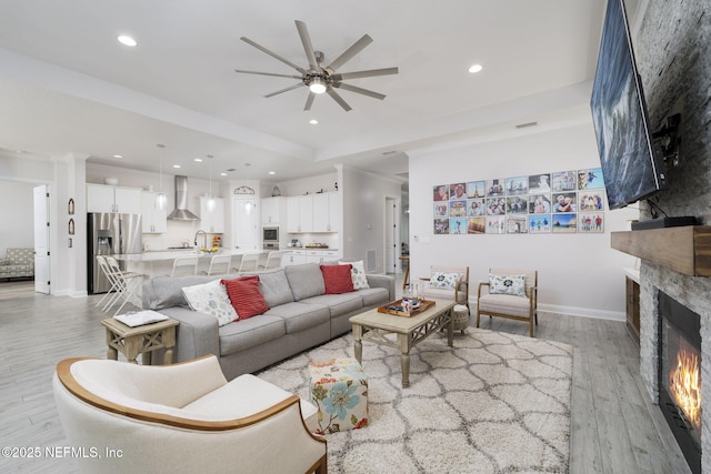 living room with a stone fireplace, sink, ceiling fan, crown molding, and light hardwood / wood-style flooring