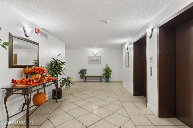 hall with light tile patterned floors, a textured ceiling, and elevator