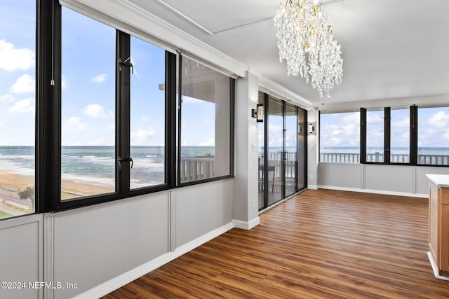 unfurnished sunroom with a view of the beach, a water view, and a notable chandelier