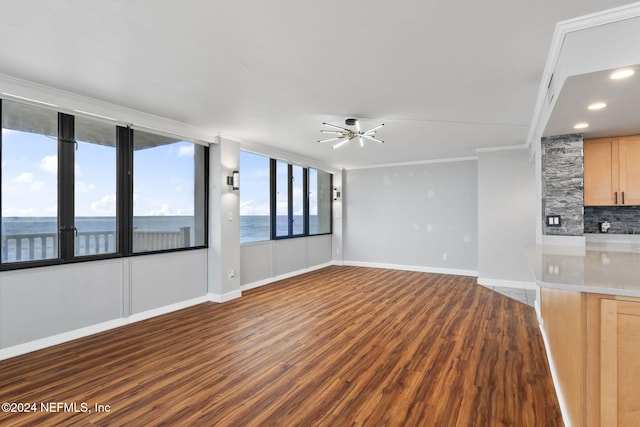 unfurnished living room with ceiling fan, dark hardwood / wood-style floors, a water view, and crown molding