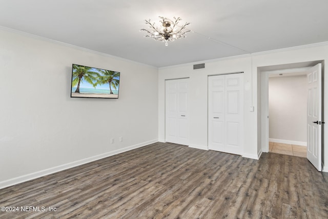 unfurnished bedroom featuring crown molding, dark hardwood / wood-style flooring, a chandelier, and two closets