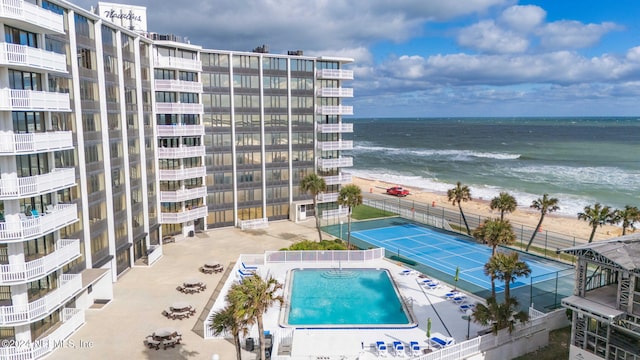 view of swimming pool with a beach view, a water view, and tennis court