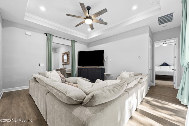 living room with a raised ceiling, dark wood-type flooring, and ornamental molding