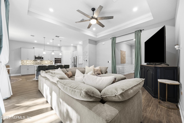 living room featuring hardwood / wood-style flooring, a raised ceiling, ceiling fan, and ornamental molding