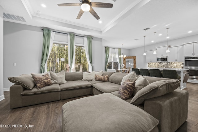 living room with dark hardwood / wood-style flooring, a raised ceiling, ceiling fan with notable chandelier, and crown molding