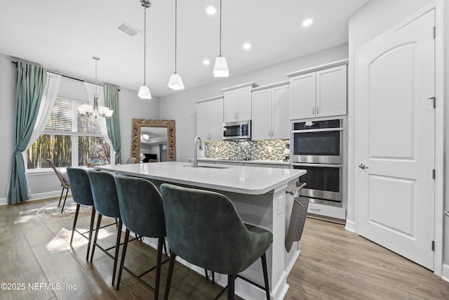 kitchen with white cabinetry, sink, stainless steel appliances, an island with sink, and pendant lighting