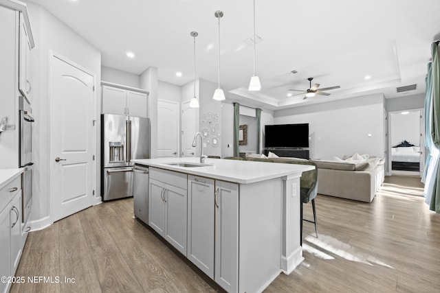 kitchen featuring ceiling fan, sink, stainless steel appliances, an island with sink, and a tray ceiling