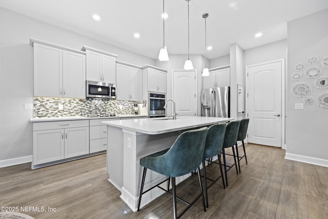 kitchen with hardwood / wood-style floors, a kitchen island with sink, sink, appliances with stainless steel finishes, and decorative light fixtures