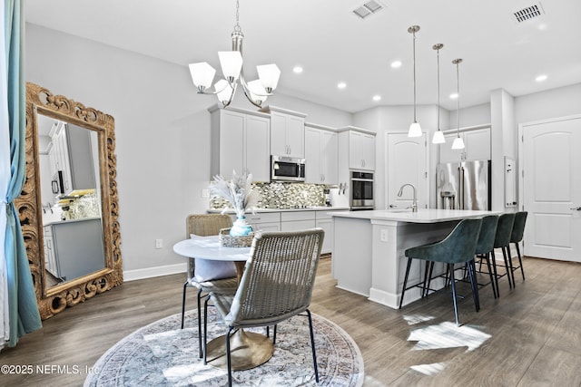 kitchen featuring white cabinets, stainless steel appliances, hanging light fixtures, and a center island with sink