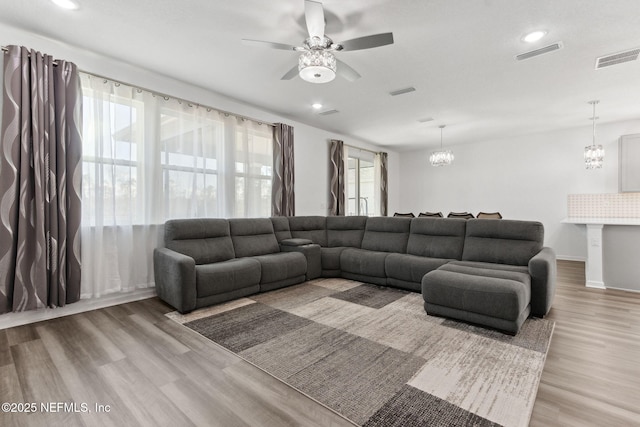 living room with light wood-type flooring and ceiling fan with notable chandelier