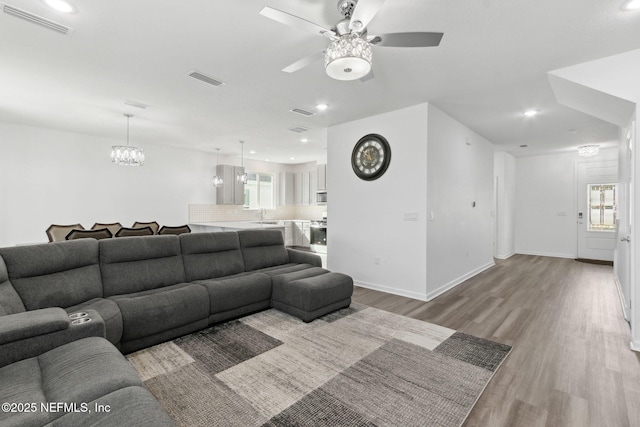 living room featuring ceiling fan with notable chandelier, light hardwood / wood-style floors, and a healthy amount of sunlight