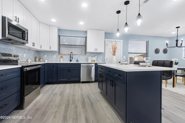 kitchen with sink, stainless steel appliances, decorative light fixtures, white cabinets, and light wood-type flooring