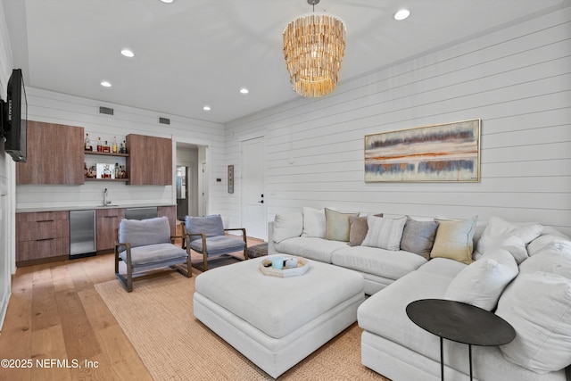 living room with wooden walls, light hardwood / wood-style flooring, sink, and an inviting chandelier