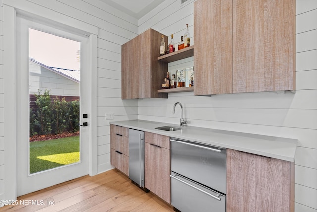 kitchen featuring a healthy amount of sunlight, light wood-type flooring, wooden walls, and sink