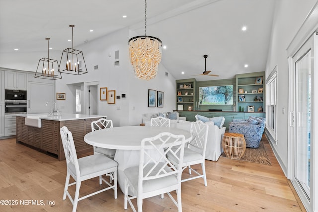 dining room featuring ceiling fan with notable chandelier, light hardwood / wood-style floors, high vaulted ceiling, and sink